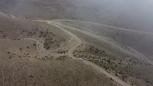 Flight through cloud, lone truck drives on twisted arid dirt road
