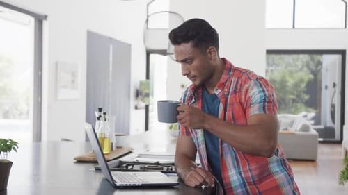 Man Drinks Coffee and Works at Home on Laptop