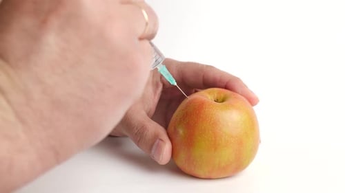Syringe Injecting Liquid into Apple on White Background