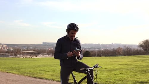 mature man does sports on a bicycle, stops to rest and look at messages on his smart phone