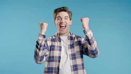 Excited Young Man Cheers Against Blue Background