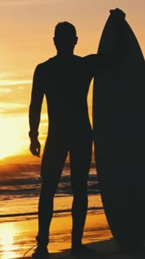 Silhouette of Man Standing with Surfboard on Beach at Sunset