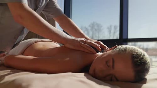 Thérapie relaxante de massage du dos aux pierres chaudes dans un cadre de spa tranquille avec une femme paisible allongée en massage