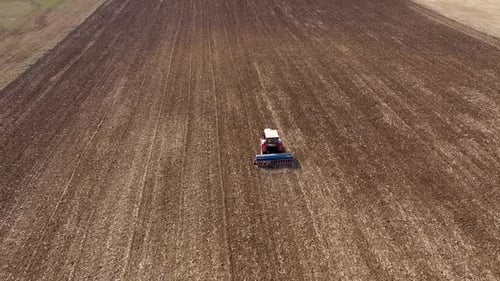 Slow motion aerial view of tractor seeding-sowing crops at agricultural field. Soil loosening