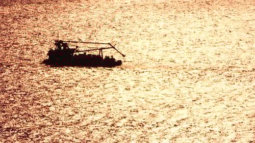 Tug Boat Pulls a Barge Loaded with Harbor Cranes Across Calm Seas at Golden Sunset Aerial View