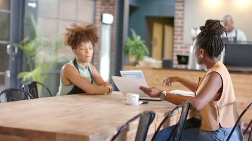 Consultora afroamericana mostrando páginas, cliente revisando con una computadora portátil en un café para una entrevista
