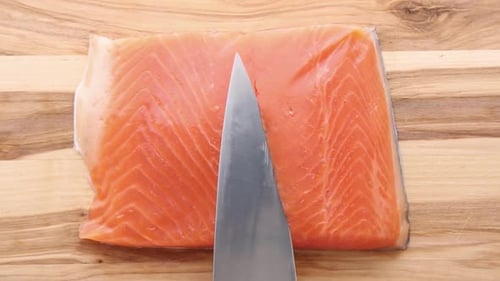 Fresh Salmon Fillet Being Cut Into Portions On Wooden Board
