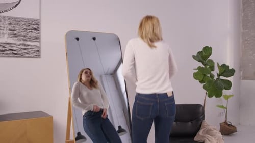 Overweight Mature Woman Trying to Button Up Tight Pants in Front of Mirror