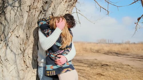 Couple warmly kisses by tree in romantic spring setting.