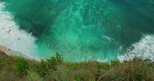 Top down view of clear turquoise tropical water hitting the steep cliff edge on Bali coastline