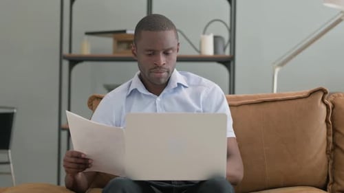 Man Reviews Documents on Laptop at Home