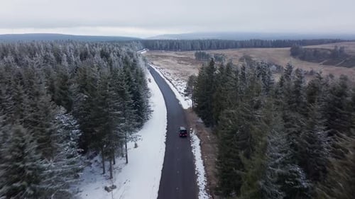 Luftaufnahme einer Autofahrt auf einer kurvenreichen Straße durch einen verschneiten Wald, Winterreise und Reisen