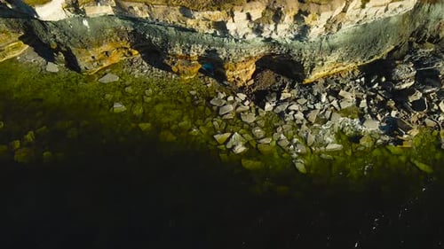 Aerial Top Down View Flying Along Rugged Cliff Caves and Rocky Shoreline