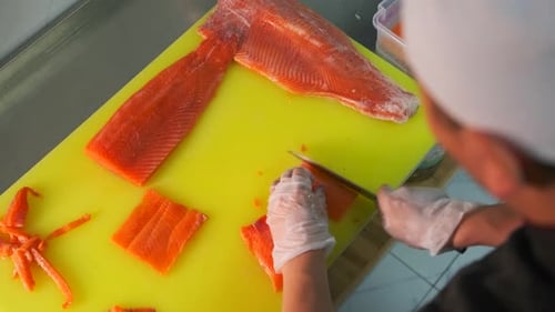 Close-up of asian sushi chef in gloves slices fresh salmon fish fillet at sushi bar. Top view.