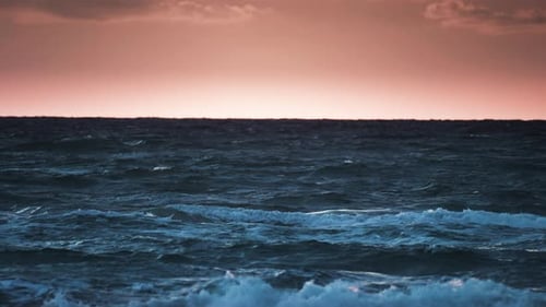 Beautiful sunset over the sea. Waves roll on the coast. Slow-motion, pan left.