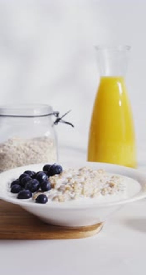 Pouring Milk over Oatmeal Bowl with Blueberries