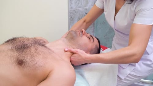 female therapist massaging shoulders and neck of male customer in spa salon