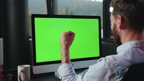 A Man is Diligently Working at His Computer with a Green Screen Background for Various Uses