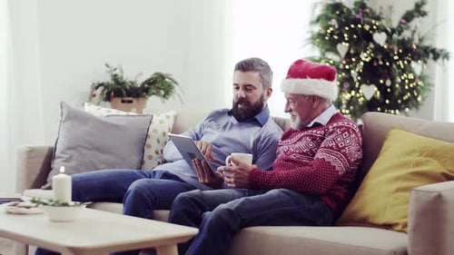 A Senior Father and Adult Son with Tablet Sitting on a Sofa
