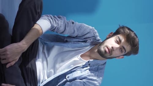 Contemplative Man Sits Thoughtfully in Front of Blue Wall