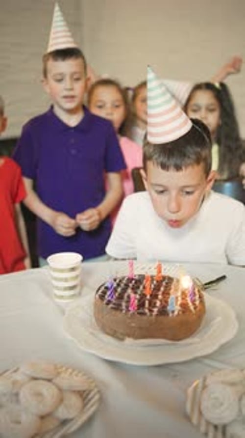 Vídeo vertical: Aniversariante em um boné festivo, apagando as velas de um bolo de aniversário e seus