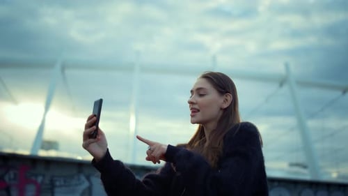 Cheerful girl making self video for blog on cellphone in bustling city street