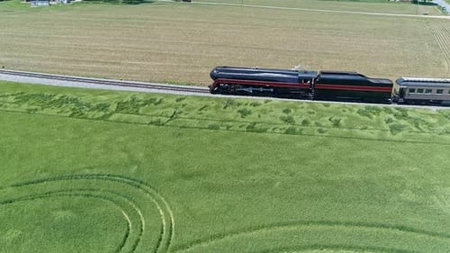 An Aerial Parallel View of an Antique Steam Passenger Train Traveling Thru Farmlands on a Sunny Day