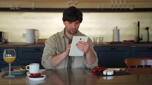 Man Works on a Tablet Uses Free Internet Access Drinks Orange Juice and Eats a Delicious Breakfast