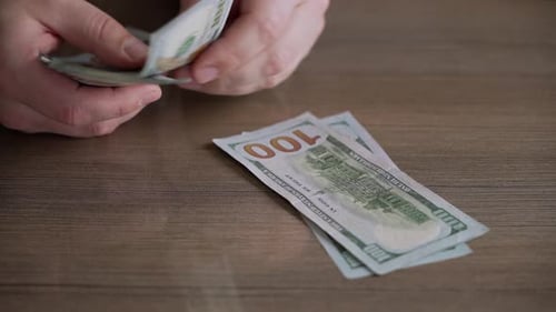 Close up men's hands count money, dollar bills, stacking on wooden table.