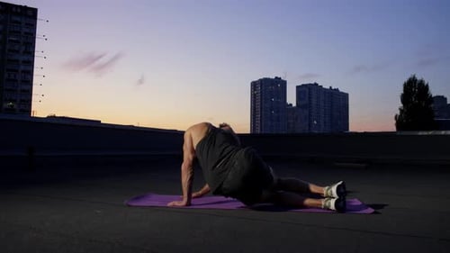A Man is Doing Fitness on a Rooftop in the City at Sunset