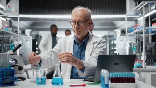 Un chercheur âgé inspecte la clarté d'un liquide bleu dans un tube à essai à l'aide d'un ordinateur portable