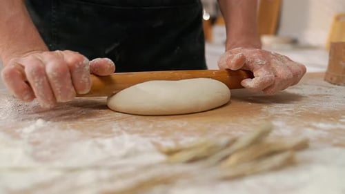 Hands rolling dough with a wooden rolling pin