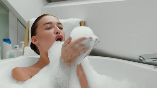 Woman Lying in Bubble Bath Blowing Soap