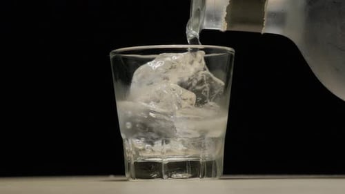 Pouring alcohol with ice on shot glass. close up