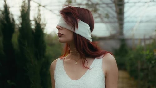 cinematic video of woman in white dress and blindfold looking around