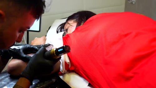 Tattoo artist finishing a dog tattoo on the arm of a woman in the studio