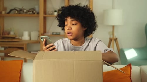 Woman Opening Shipping Box with Smartphone at Home