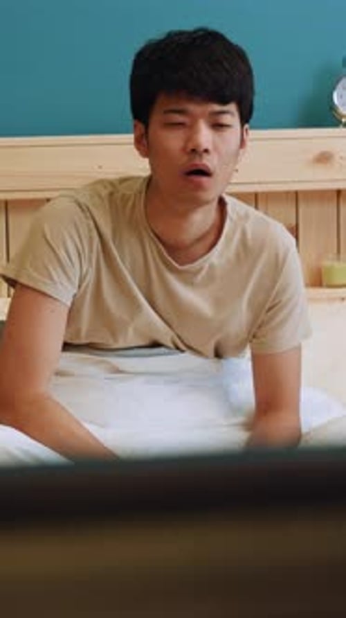 A Young Man Enjoys Watching Television in His Cozy and Comfortable Bedroom Space