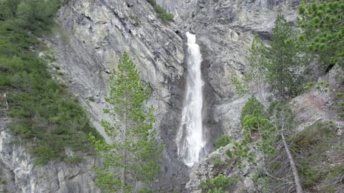 Aerial drone footage slowly flying through a tree canopy towards a dramatic waterfall as it cascades