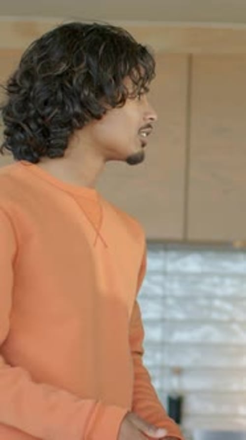 Vertical video: Turning man in orange top hearing voice right in kitchen moving lettuce, copy space