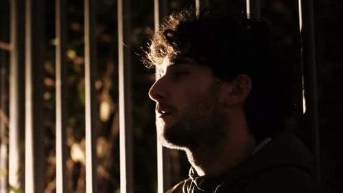sense of guilt -young thoughtful man in the dark leaning against a gate thinking