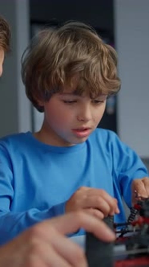 Young Boy in Blue Shirt Concentrating on Assembling a Small Toy Vehicle with Wheels and Wires at a