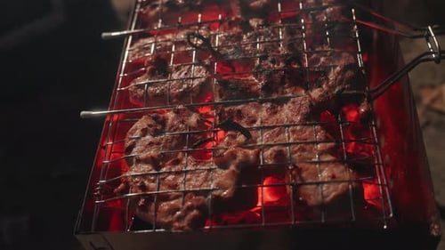 Rustikale Grillszene im Freien, Lagerfeuer, Kochen von saftigem, gewürztem Fleisch am Abend, in der Outdoor-Küche