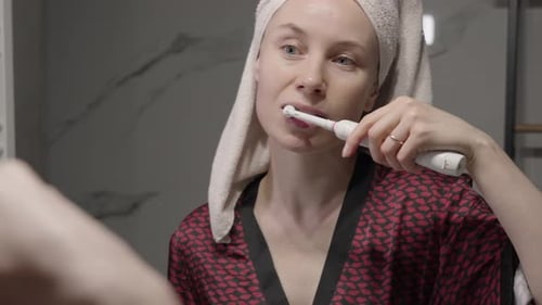 Mujer cepillándose los dientes con un cepillo de dientes eléctrico en el baño