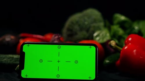 Closeup Green Screen of Smartphone at Background of Homegrown Organic Vegetables at Black Background
