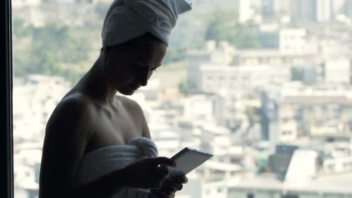 Woman in towel using tablet by window