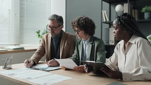 Three Multiethnic Colleagues Discussing Documents At Office Table