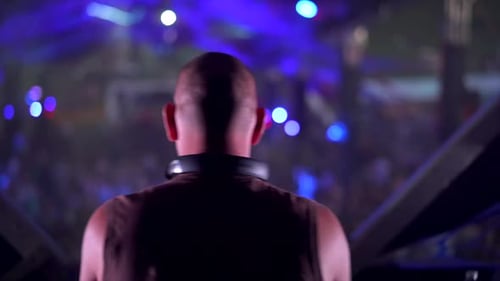 Rear shot of male disk jockey with baldness put on some music in nightclub stage,close up.
