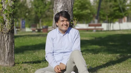 Young Adult Smiling, Sitting by Tree in Park