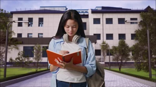 Girl Student Smiling And Taking Note On Notebook in Front of a School Building